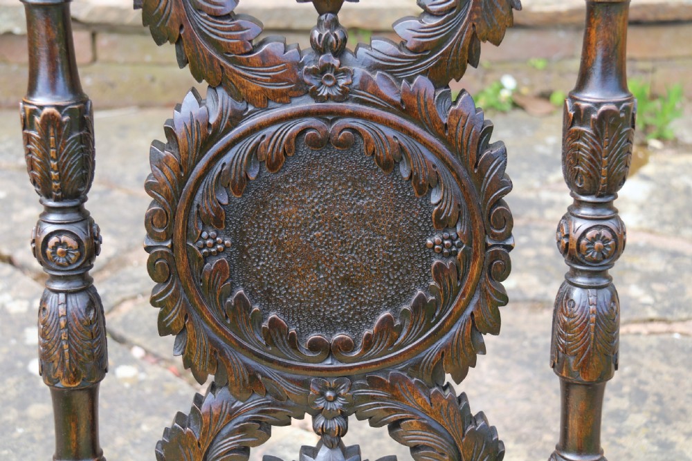 A 19th-century high-backed dark walnut chair featuring intricate floral, bird, and acanthus leaf wood carvings and a patterned upholstered seat. View X