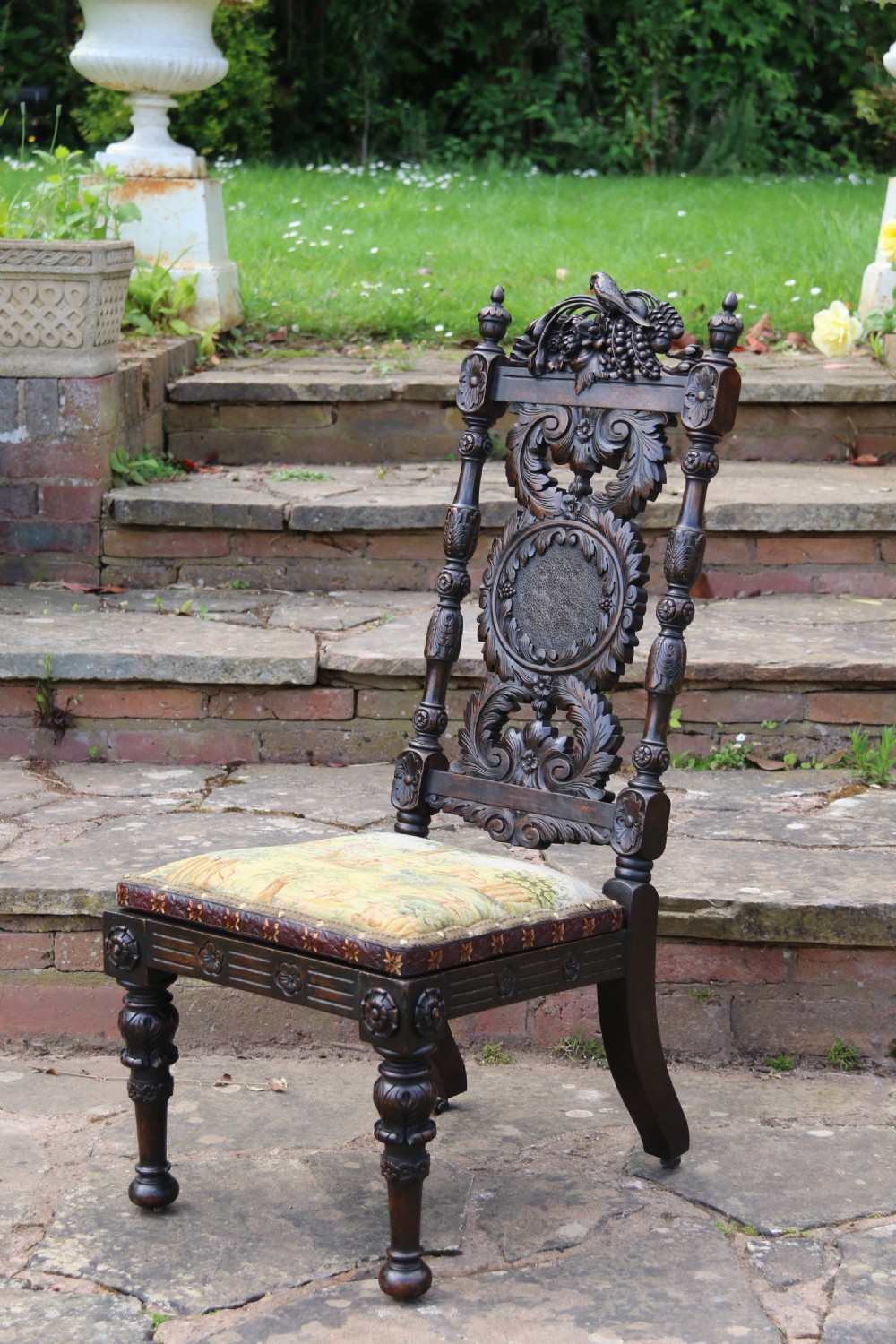 A 19th-century high-backed dark walnut chair featuring intricate floral, bird, and acanthus leaf wood carvings and a patterned upholstered seat. View XII