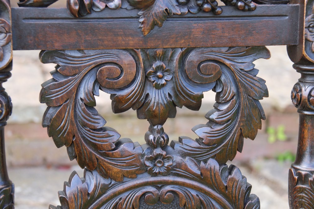 A 19th-century high-backed dark walnut chair featuring intricate floral, bird, and acanthus leaf wood carvings and a patterned upholstered seat. View XXII