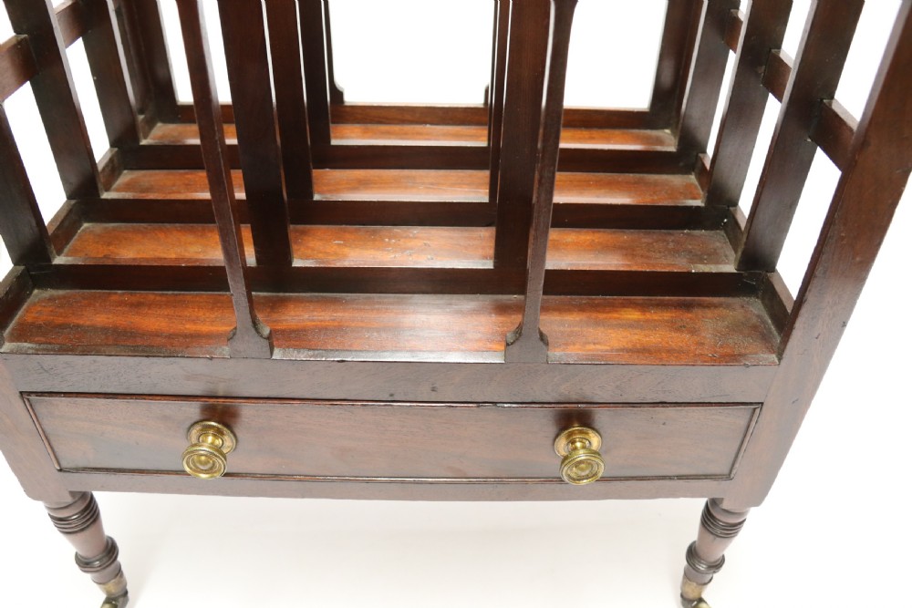 A dark mahogany George III Canterbury featuring slatted vertical partitions, a lower single drawer with brass ring handles, and turned legs resting on brass castors. View XIV