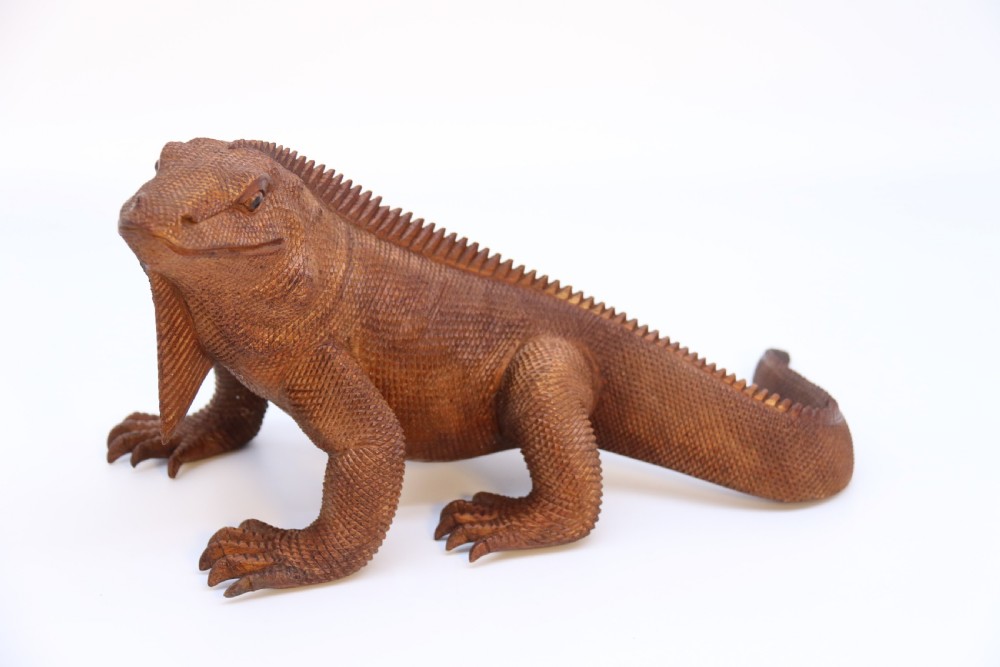 A hand-carved hardwood sculpture of an iguana featuring detailed scale patterns, a serrated dorsal crest, and a prominent dewlap in a warm brown finish.