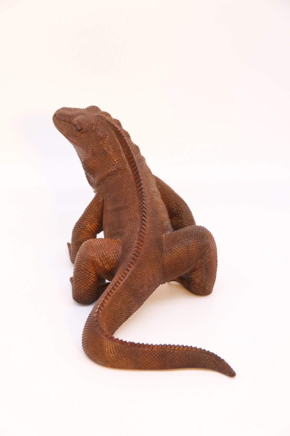 A hand-carved hardwood sculpture of an iguana featuring detailed scale patterns, a serrated dorsal crest, and a prominent dewlap in a warm brown finish. View V
