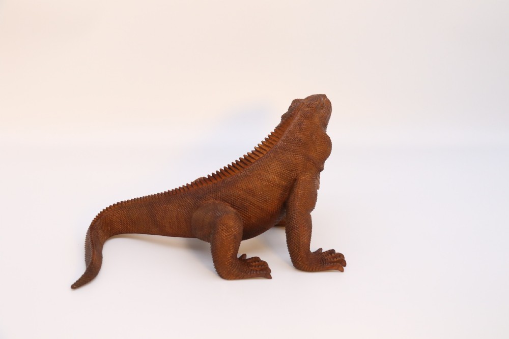 A hand-carved hardwood sculpture of an iguana featuring detailed scale patterns, a serrated dorsal crest, and a prominent dewlap in a warm brown finish. View VI