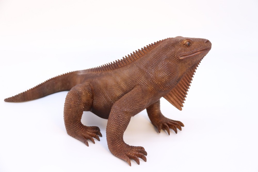 A hand-carved hardwood sculpture of an iguana featuring detailed scale patterns, a serrated dorsal crest, and a prominent dewlap in a warm brown finish. View VIII