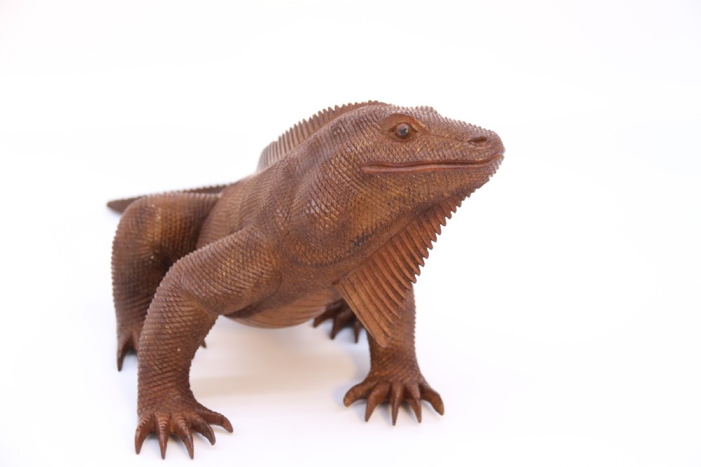 A hand-carved hardwood sculpture of an iguana featuring detailed scale patterns, a serrated dorsal crest, and a prominent dewlap in a warm brown finish. View IX