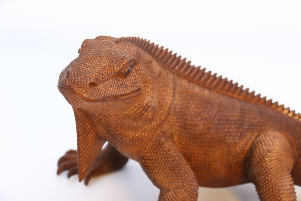 A hand-carved hardwood sculpture of an iguana featuring detailed scale patterns, a serrated dorsal crest, and a prominent dewlap in a warm brown finish. View X