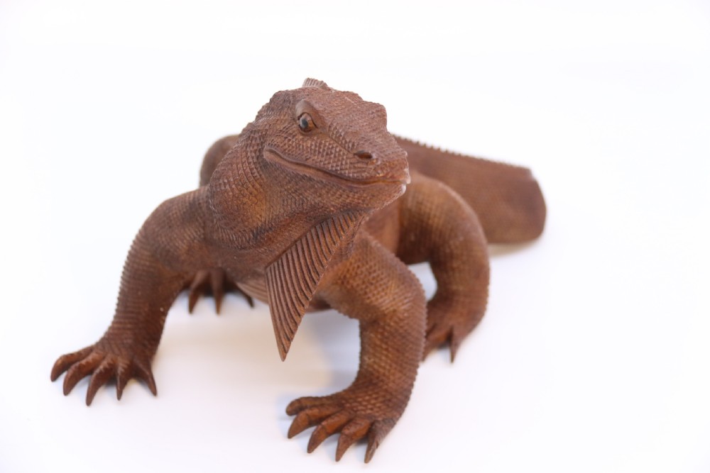 A hand-carved hardwood sculpture of an iguana featuring detailed scale patterns, a serrated dorsal crest, and a prominent dewlap in a warm brown finish. View XI