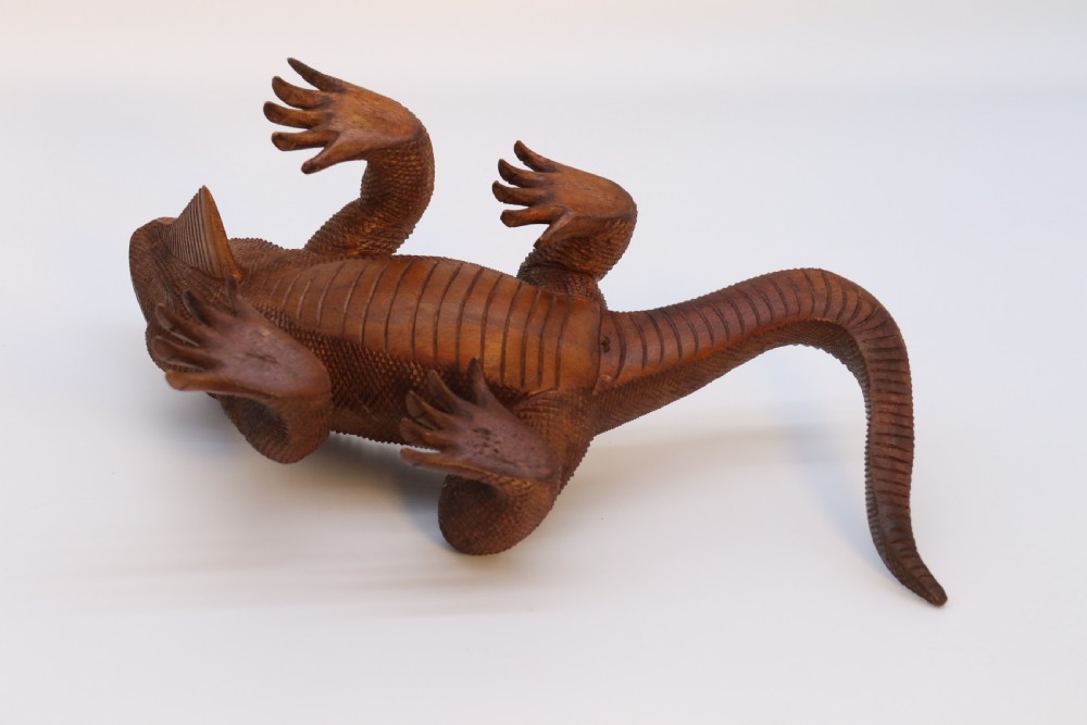 A hand-carved hardwood sculpture of an iguana featuring detailed scale patterns, a serrated dorsal crest, and a prominent dewlap in a warm brown finish. View XVII