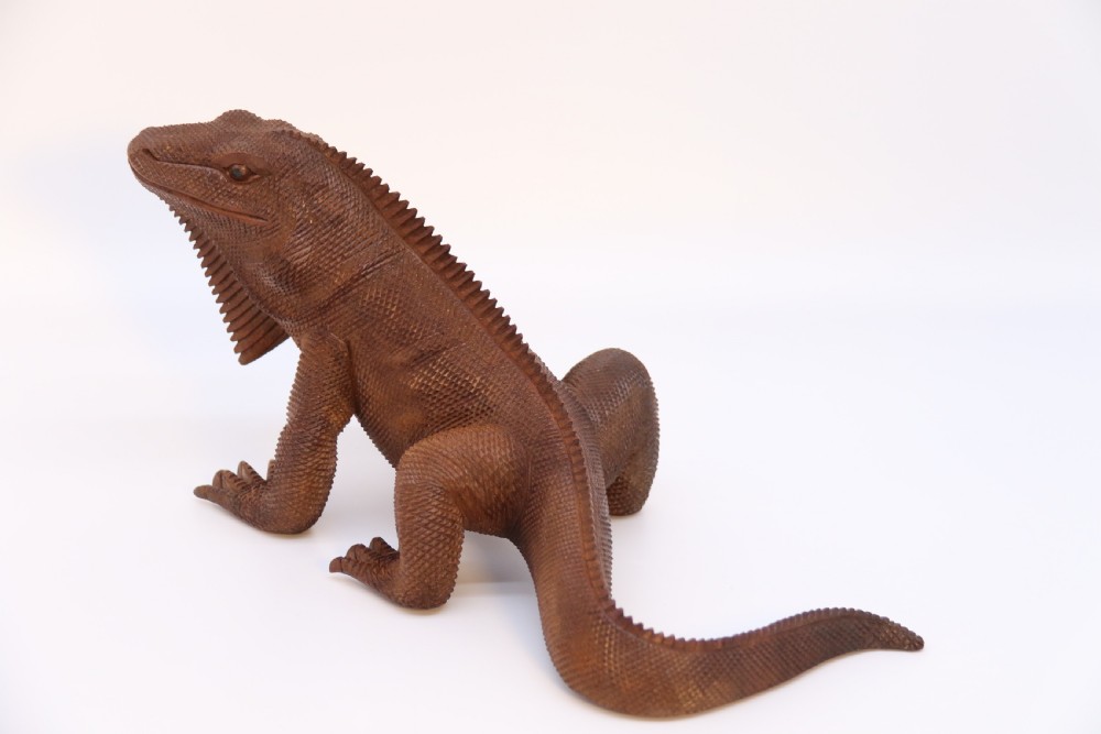 A hand-carved hardwood sculpture of an iguana featuring detailed scale patterns, a serrated dorsal crest, and a prominent dewlap in a warm brown finish. View XIX