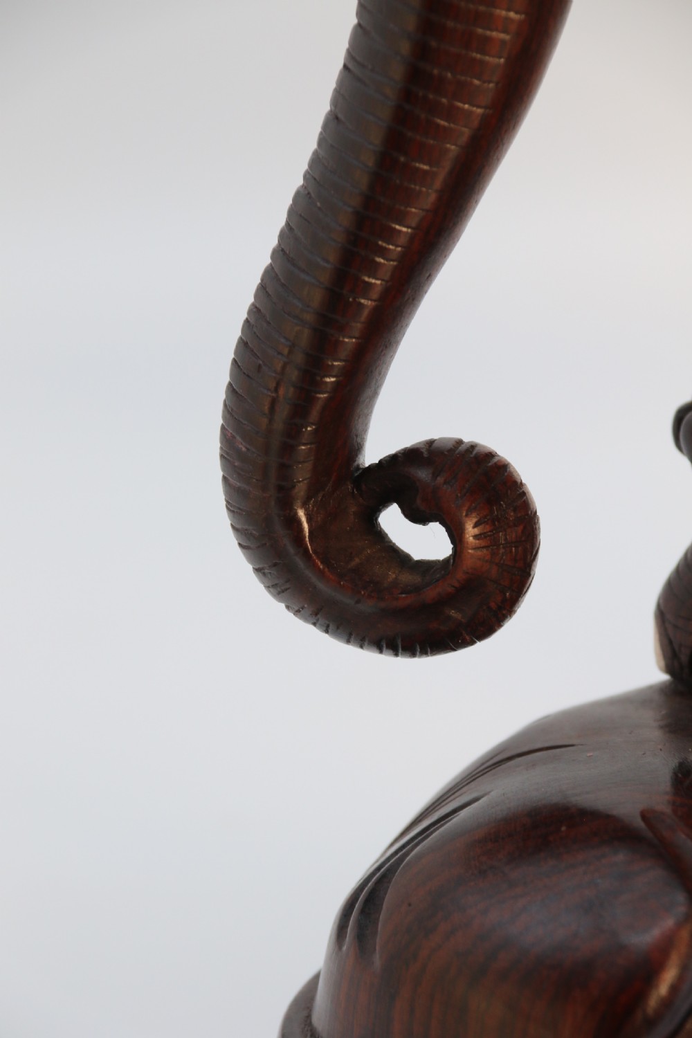 A dark hardwood sculpture depicting a ceremonial elephant adorned with decorative drapery accompanied by three mahouts on an integrated wooden base. View II