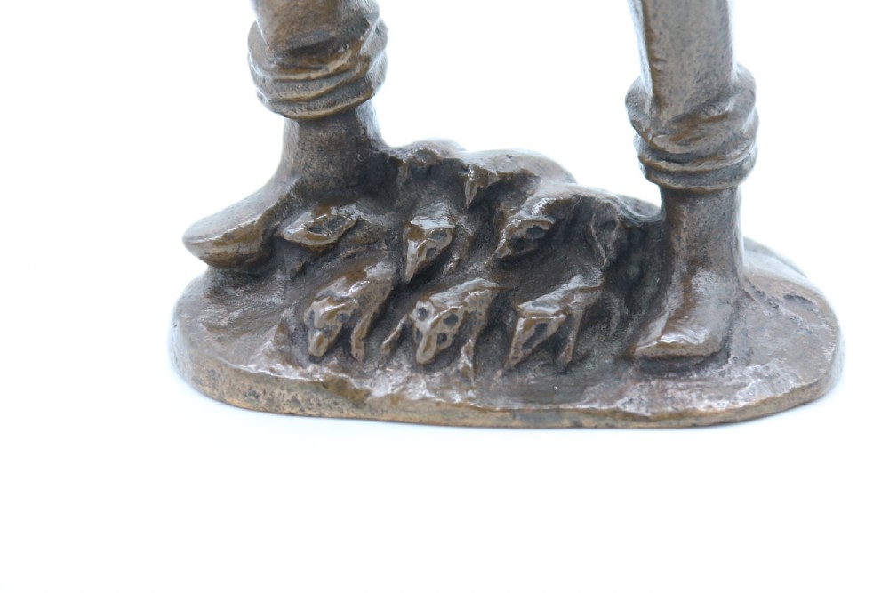 A dark brown patinated bronze statuette depicting a figure in historic costume playing a pipe while standing on a textured base. View IX