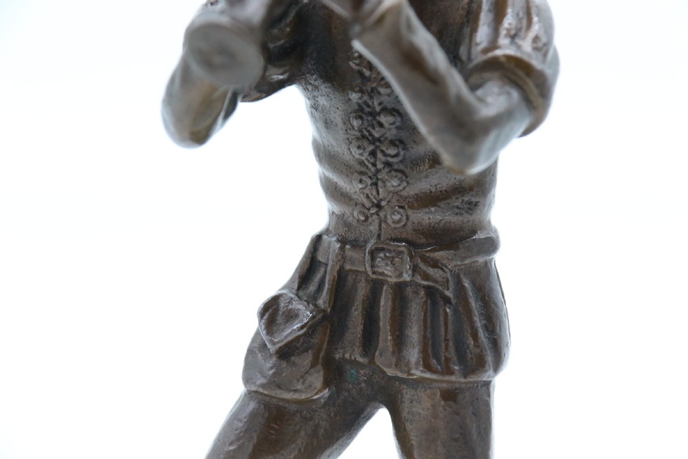 A dark brown patinated bronze statuette depicting a figure in historic costume playing a pipe while standing on a textured base. View XIV