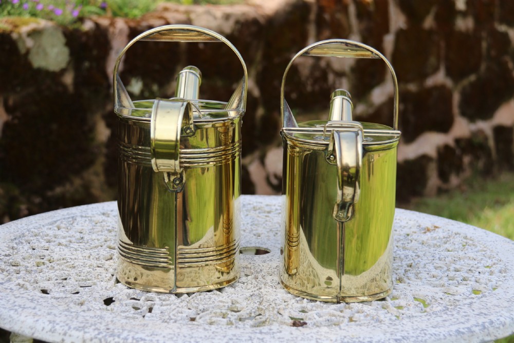 A pair of polished 19th-century brass watering cans in differing sizes featuring reeded cylindrical bodies, arched top handles, and angled spouts. View III