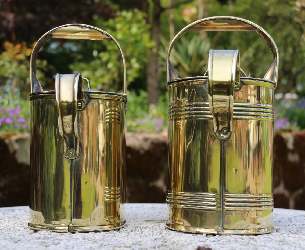 A pair of polished 19th-century brass watering cans in differing sizes featuring reeded cylindrical bodies, arched top handles, and angled spouts. View XX