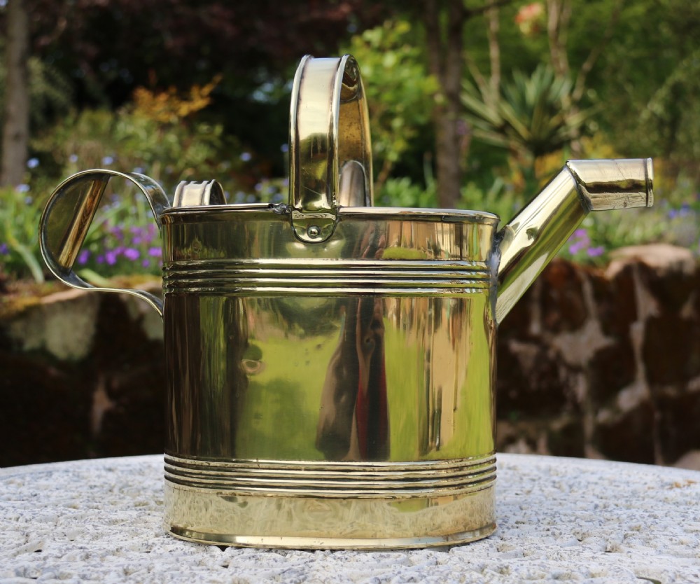 A pair of polished 19th-century brass watering cans in differing sizes featuring reeded cylindrical bodies, arched top handles, and angled spouts. View XXI