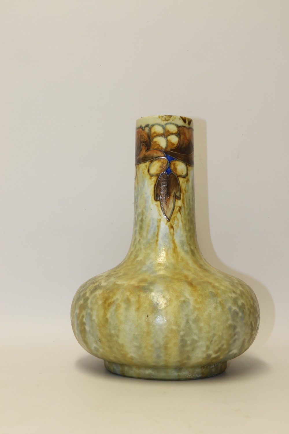 An English Cranston art pottery vase with a bulbous base, cylindrical neck, and a mottled yellow and brown glaze featuring a stylised floral motif. View IX