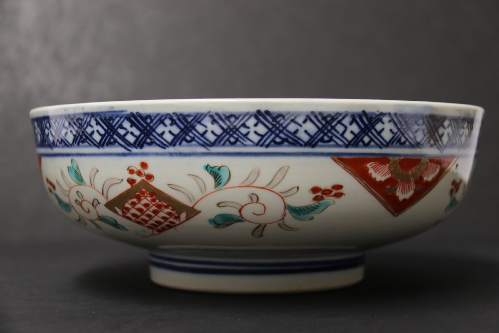A round hand-painted Japanese porcelain bowl featuring underglaze blue geometric rim borders, iron-red floral panel motifs, and gilded details on a white background. View II
