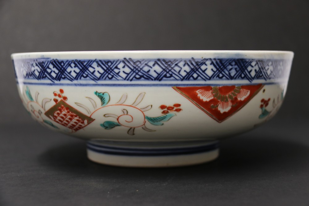 A round hand-painted Japanese porcelain bowl featuring underglaze blue geometric rim borders, iron-red floral panel motifs, and gilded details on a white background. View III