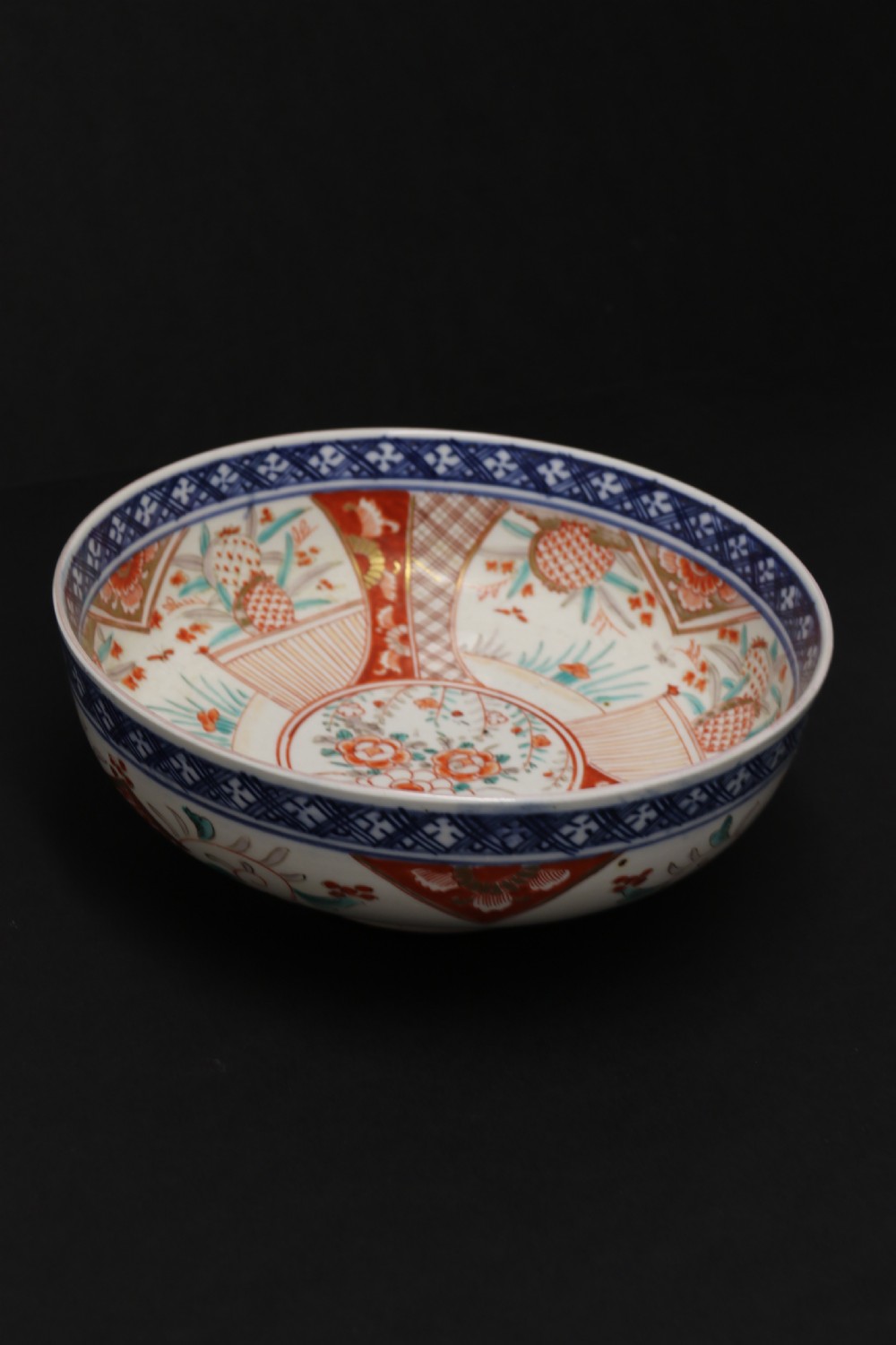 A round hand-painted Japanese porcelain bowl featuring underglaze blue geometric rim borders, iron-red floral panel motifs, and gilded details on a white background. View VII