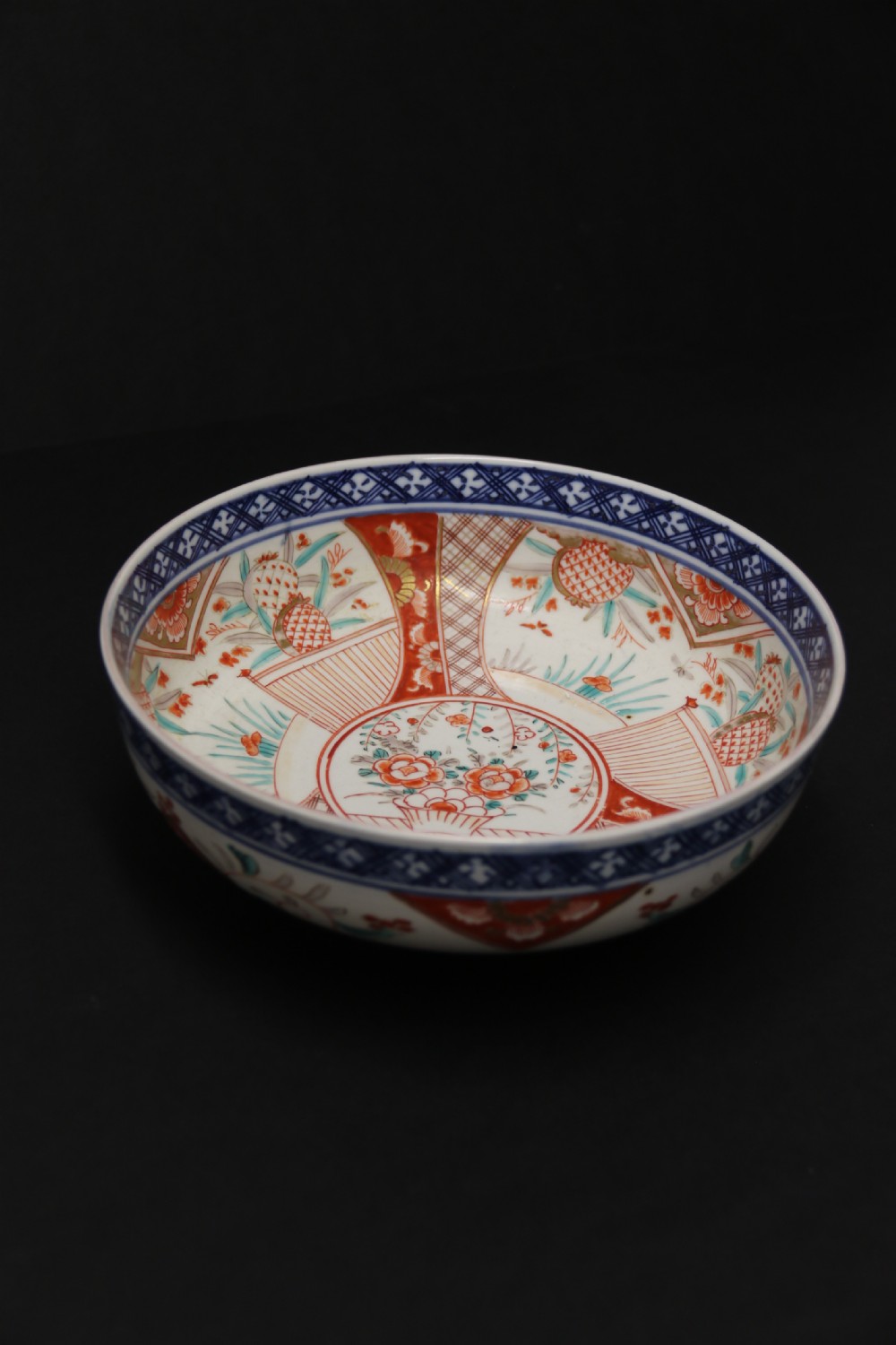 A round hand-painted Japanese porcelain bowl featuring underglaze blue geometric rim borders, iron-red floral panel motifs, and gilded details on a white background. View VIII