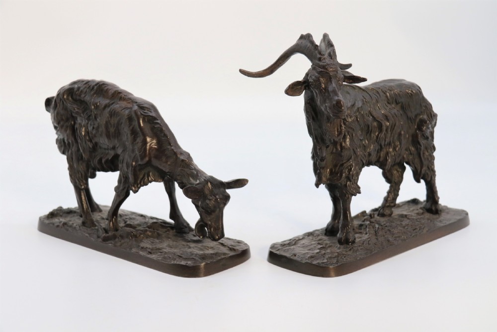 A pair of 19th-century French dark brown patinated bronze sculptures depicting a standing horned goat and a grazing goat on naturalistic bases.