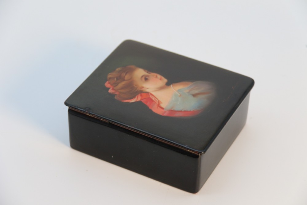 A square black lacquered box featuring a hand-painted portrait of a young woman with brown hair and a red ribbon. View V