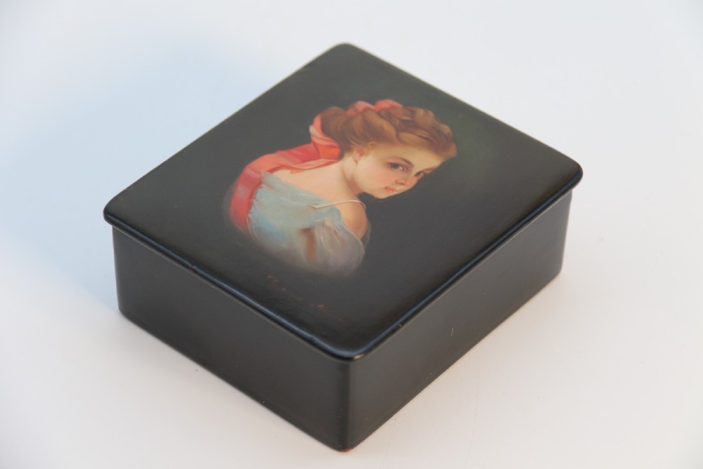 A square black lacquered box featuring a hand-painted portrait of a young woman with brown hair and a red ribbon. View VI