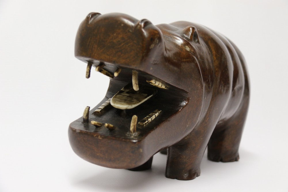 A dark brown carved hardwood hippopotamus sculpture with open mouth detailing inset bone teeth and carved body folds. View V