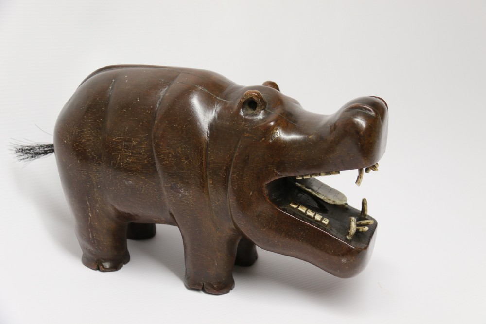 A dark brown carved hardwood hippopotamus sculpture with open mouth detailing inset bone teeth and carved body folds. View VI
