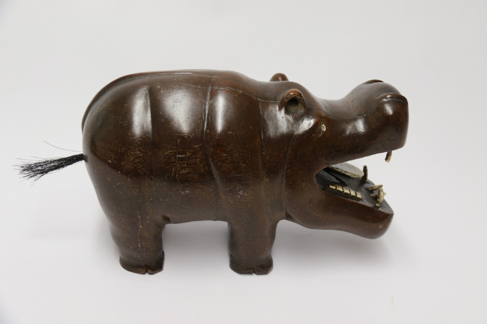 A dark brown carved hardwood hippopotamus sculpture with open mouth detailing inset bone teeth and carved body folds. View VII