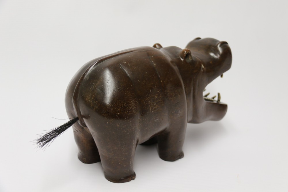A dark brown carved hardwood hippopotamus sculpture with open mouth detailing inset bone teeth and carved body folds. View VIII