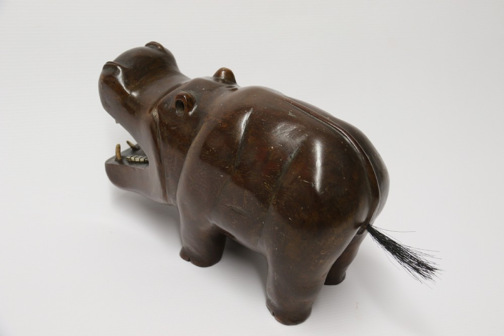A dark brown carved hardwood hippopotamus sculpture with open mouth detailing inset bone teeth and carved body folds. View X