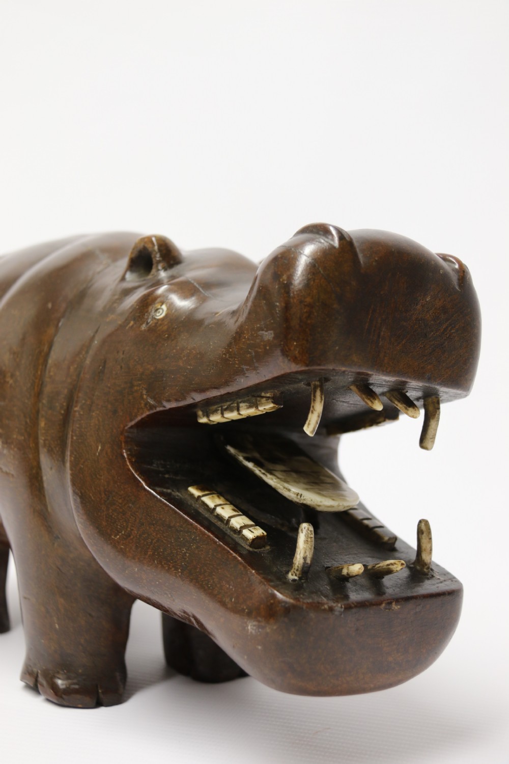 A dark brown carved hardwood hippopotamus sculpture with open mouth detailing inset bone teeth and carved body folds. View XI
