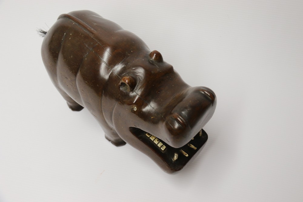 A dark brown carved hardwood hippopotamus sculpture with open mouth detailing inset bone teeth and carved body folds. View XIV