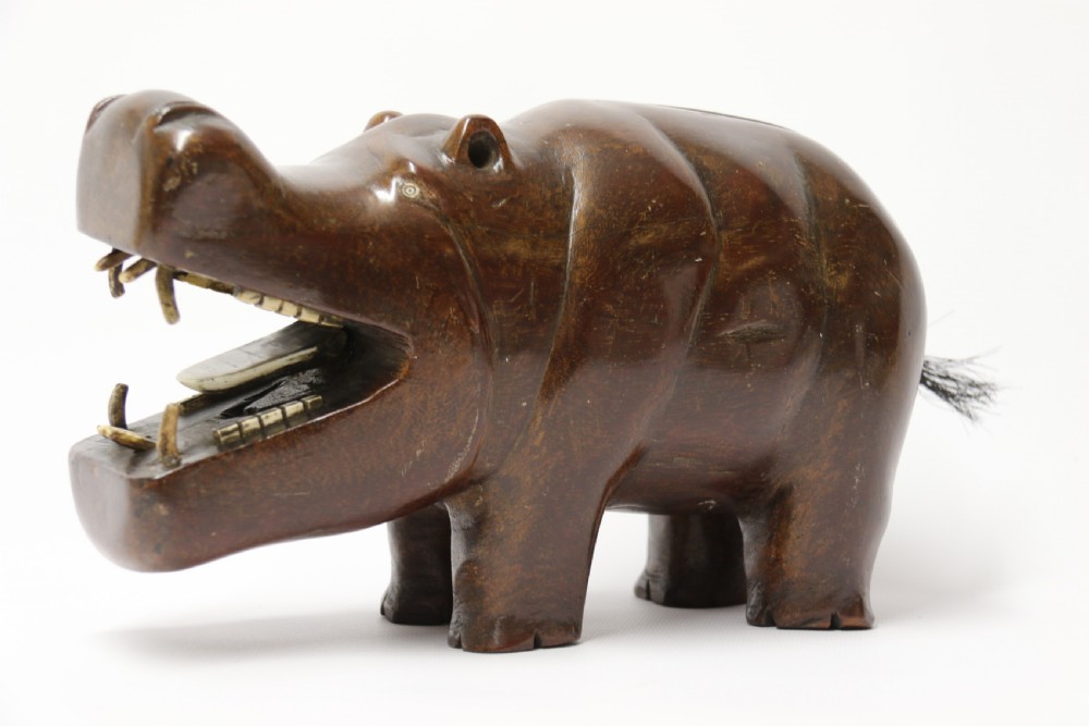 A dark brown carved hardwood hippopotamus sculpture with open mouth detailing inset bone teeth and carved body folds. View XVII