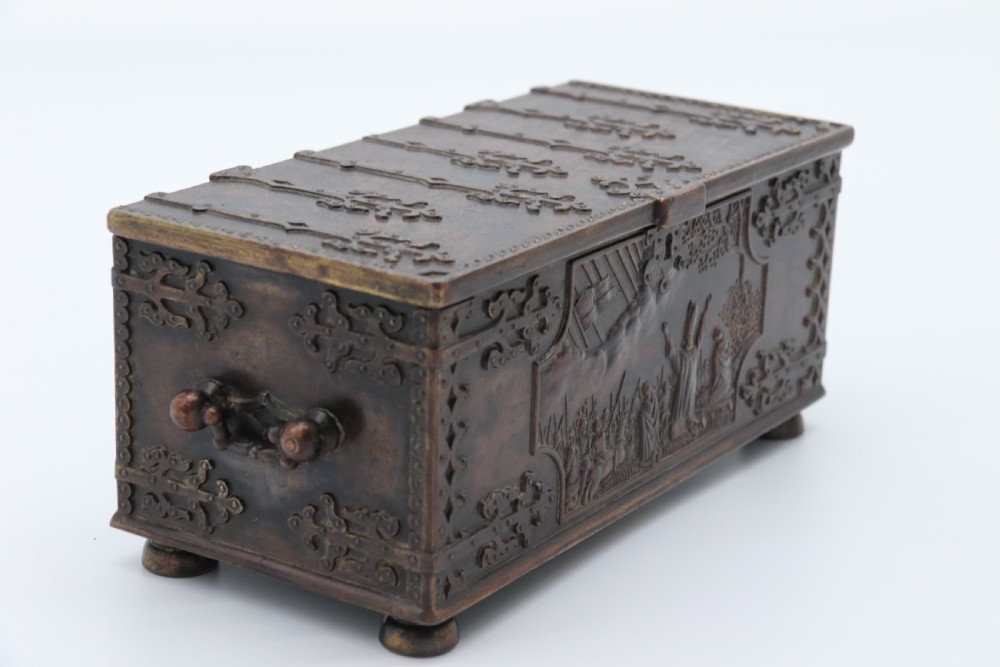 A dark brown patinated cast metal trinket box fashioned in the form of a medieval coffer with relief figures and metal strapwork details. View VII