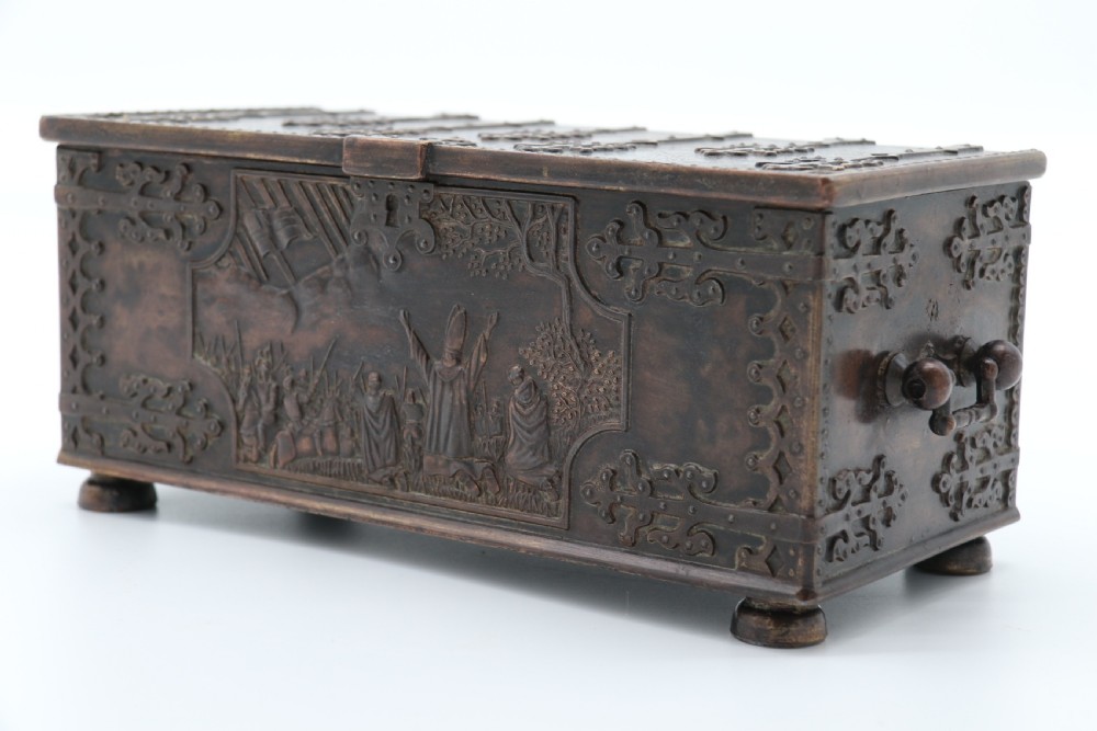 A dark brown patinated cast metal trinket box fashioned in the form of a medieval coffer with relief figures and metal strapwork details. View IX