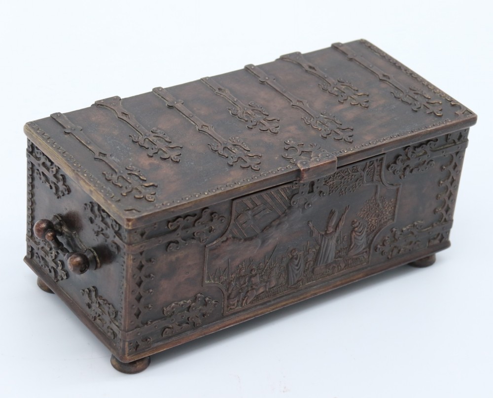 A dark brown patinated cast metal trinket box fashioned in the form of a medieval coffer with relief figures and metal strapwork details.