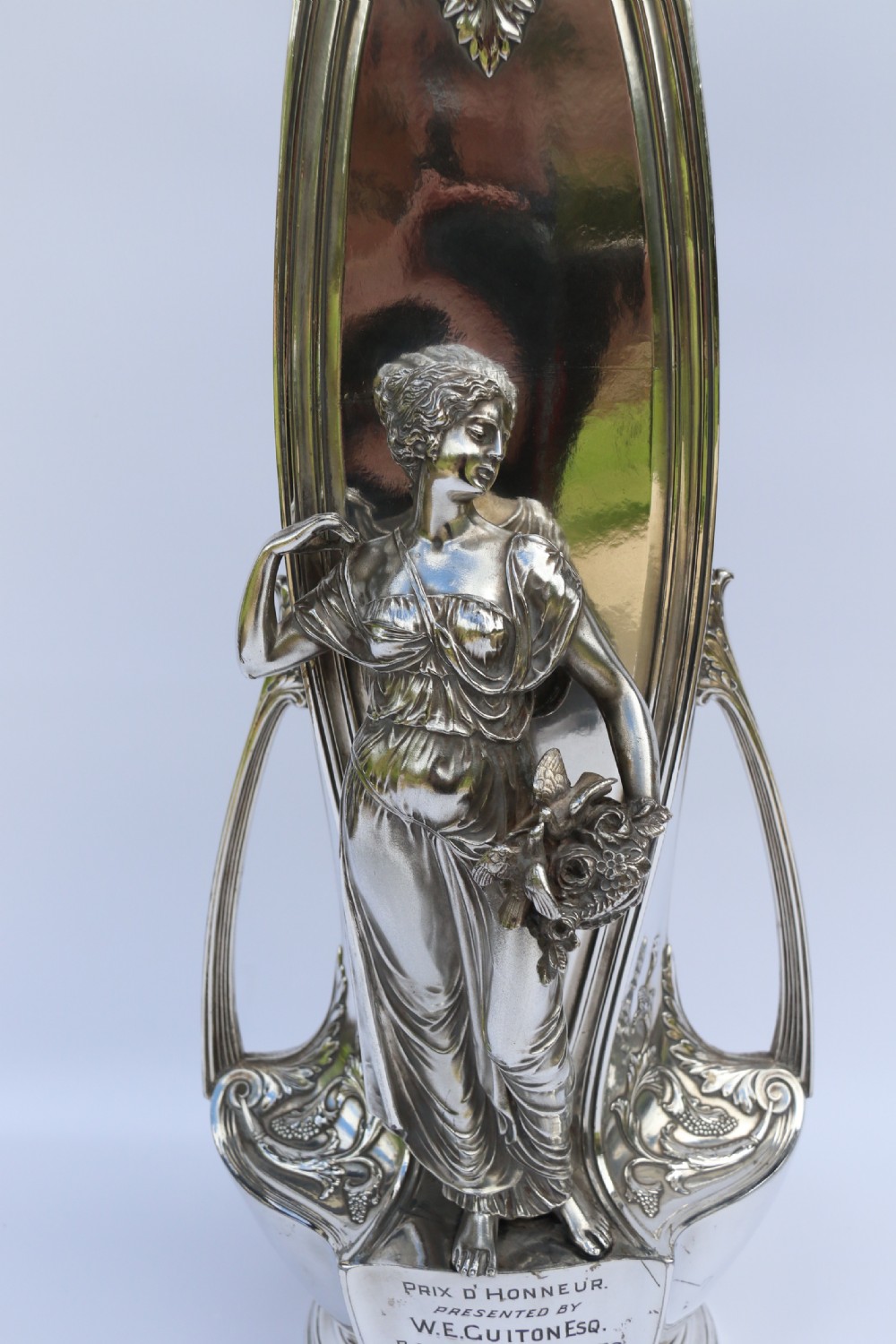 An Art Nouveau silver-plated WMF vase featuring a sculpted maiden figure in relief, sweeping organic handles, and a cut glass rim insert. View V