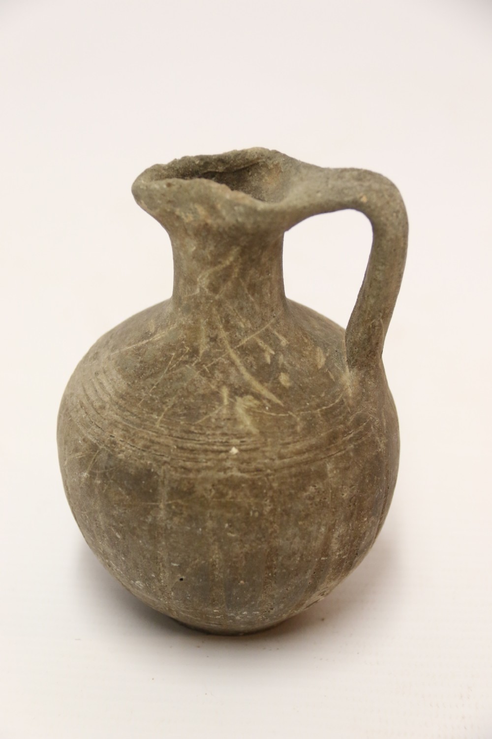 A collection of three unglazed ancient Greek terracotta vessels including a double-handled jar, a small pitcher, and a flattened flask. View X