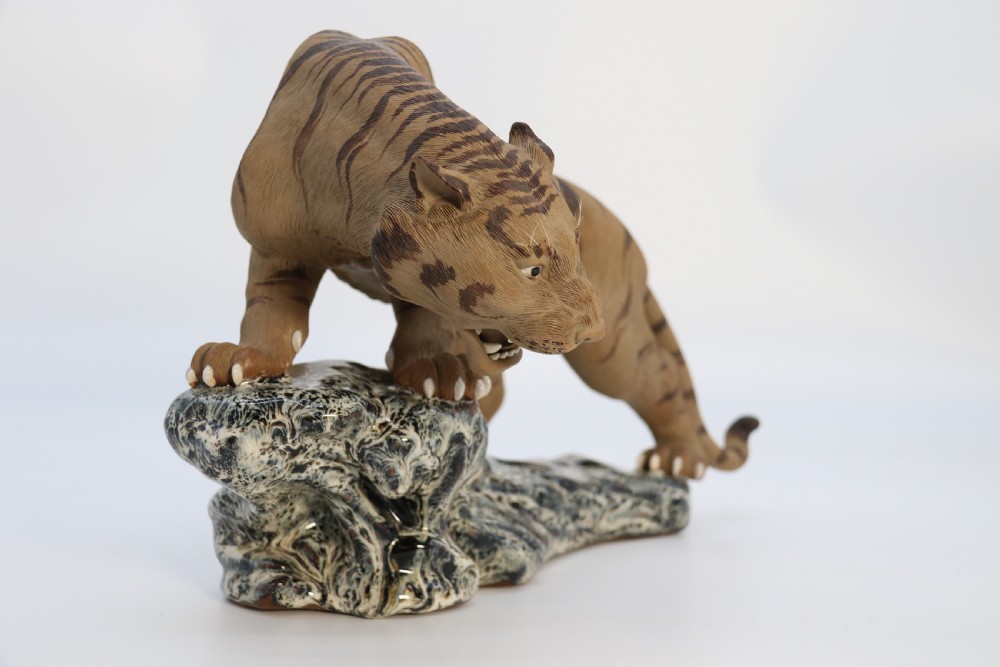 A late 19th-century Chinese Shiwan pottery tiger with incised fur texture and open jaws, standing upon a drip-glazed blue-grey rockwork base. View V
