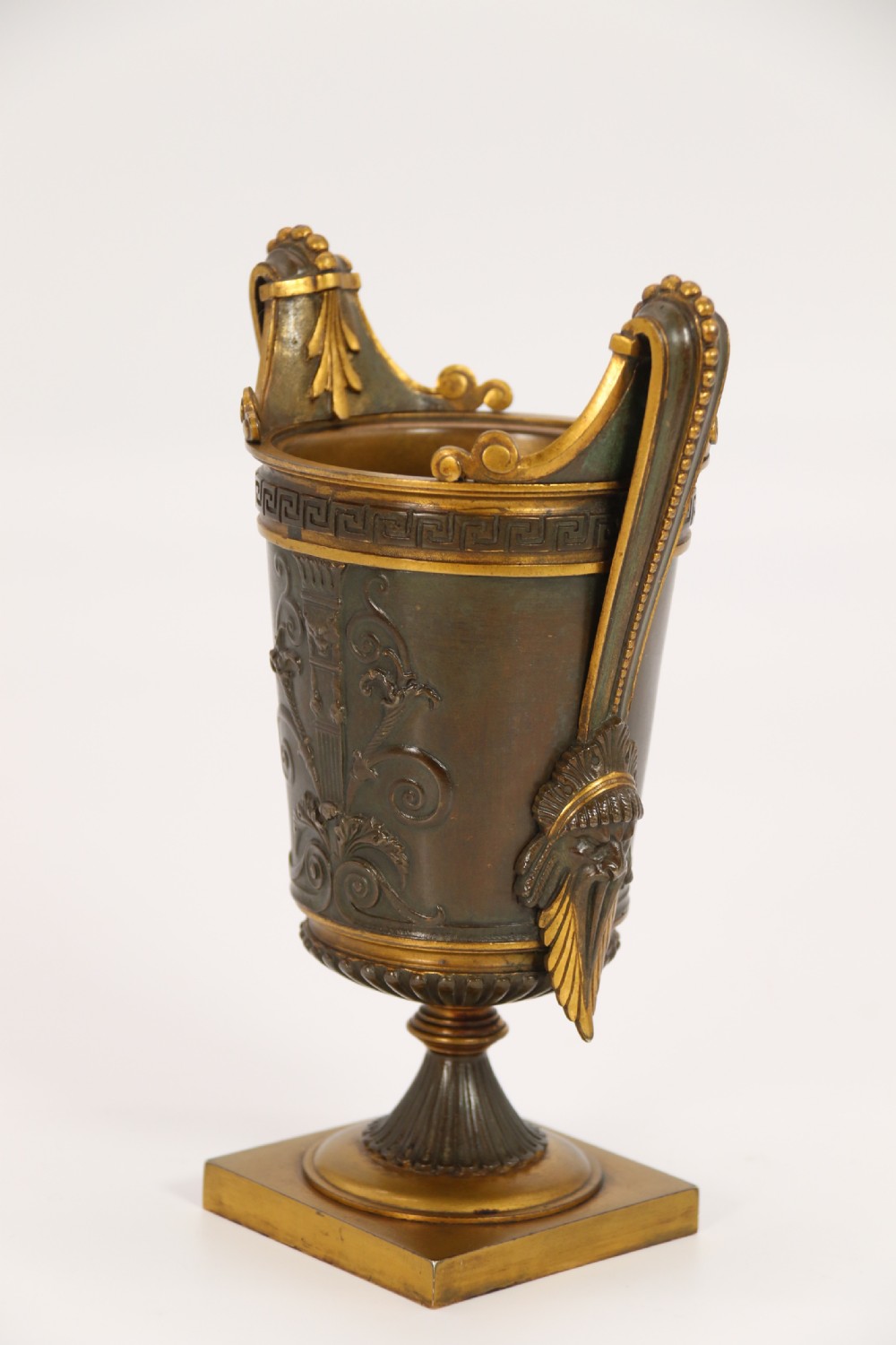 A pair of French Empire patinated and gilt bronze urns with Greek key friezes, scroll handles, and square bases. View IX