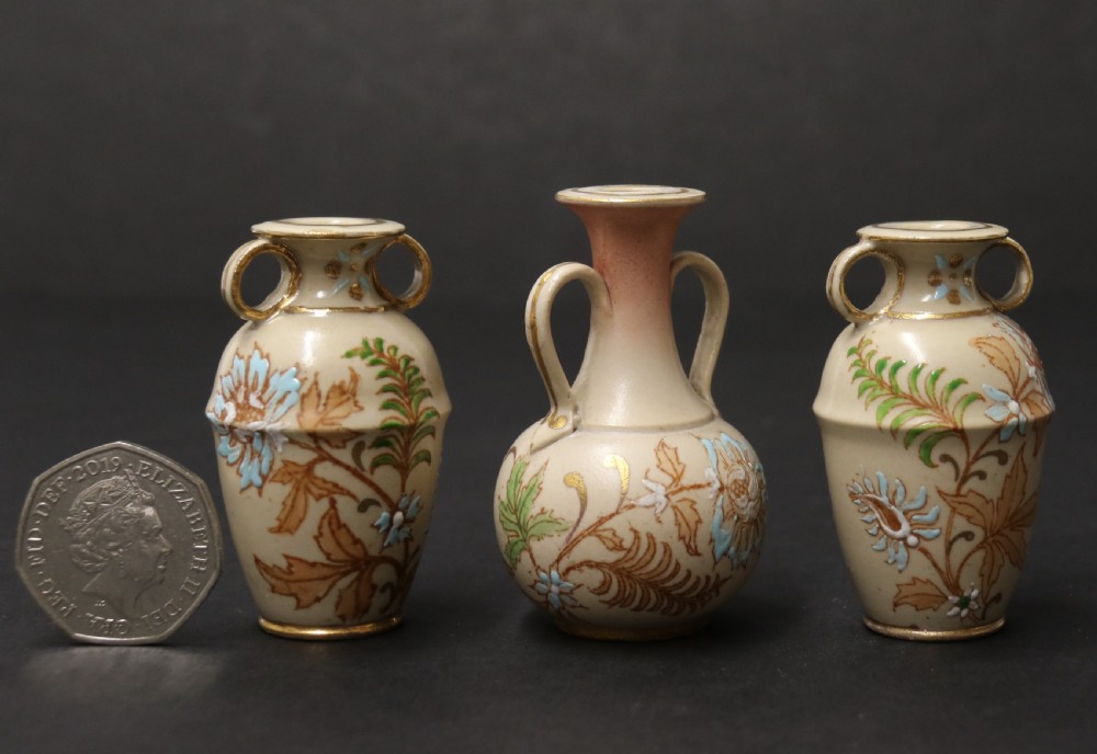 A set of three antique miniature cream ceramic vases featuring hand-painted floral motifs in blue, green, and brown with gilded highlights. View II