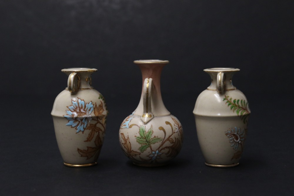 A set of three antique miniature cream ceramic vases featuring hand-painted floral motifs in blue, green, and brown with gilded highlights. View III
