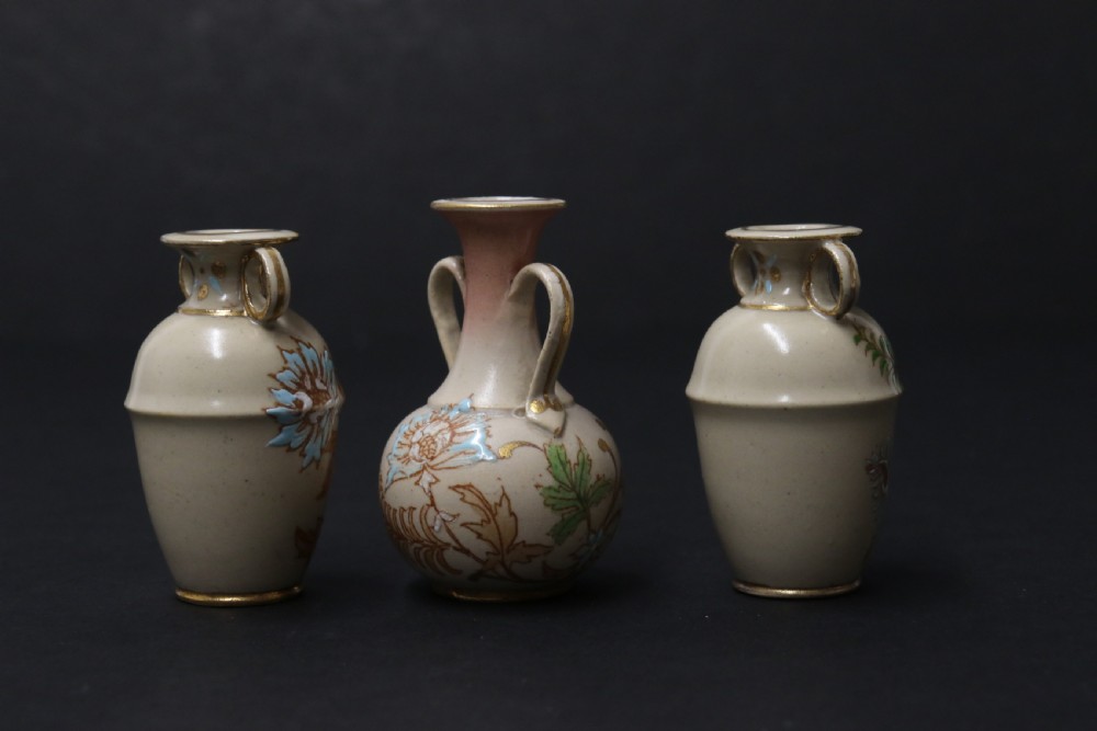 A set of three antique miniature cream ceramic vases featuring hand-painted floral motifs in blue, green, and brown with gilded highlights. View IV