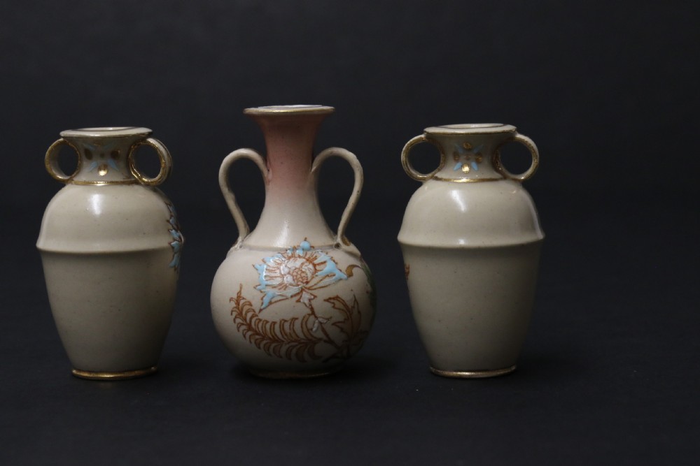 A set of three antique miniature cream ceramic vases featuring hand-painted floral motifs in blue, green, and brown with gilded highlights. View V