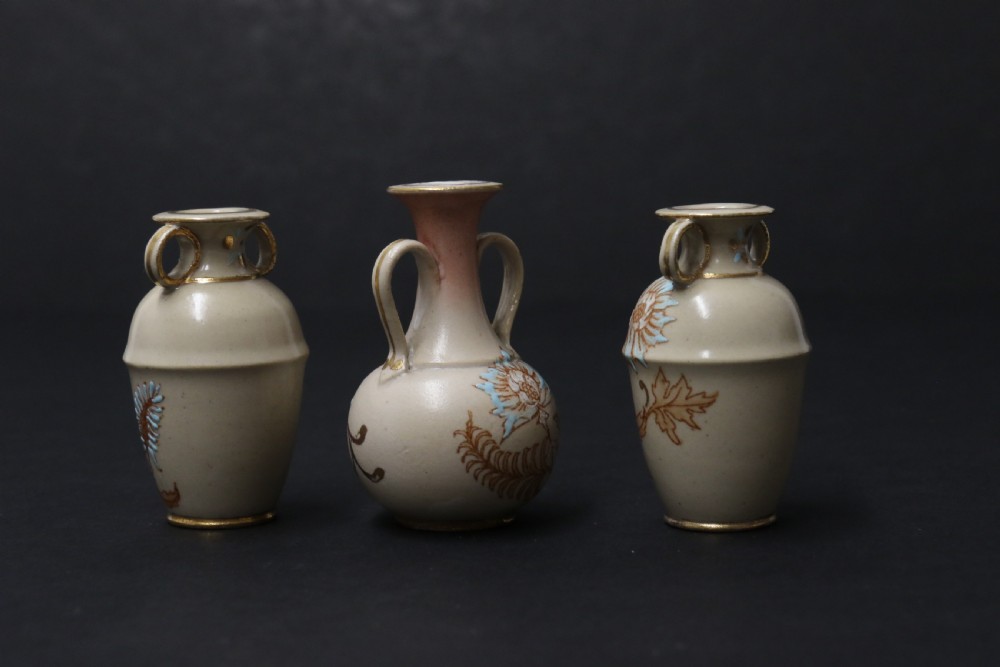 A set of three antique miniature cream ceramic vases featuring hand-painted floral motifs in blue, green, and brown with gilded highlights. View VI