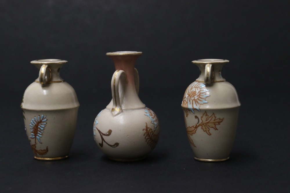 A set of three antique miniature cream ceramic vases featuring hand-painted floral motifs in blue, green, and brown with gilded highlights. View VII