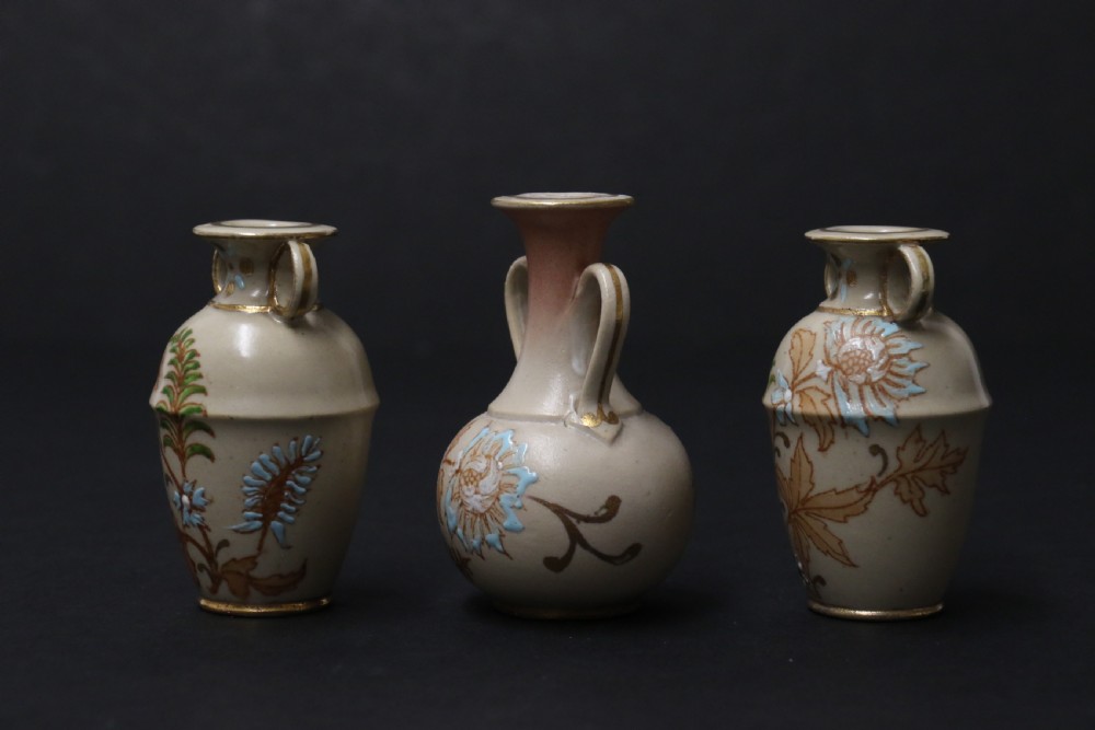 A set of three antique miniature cream ceramic vases featuring hand-painted floral motifs in blue, green, and brown with gilded highlights. View VIII