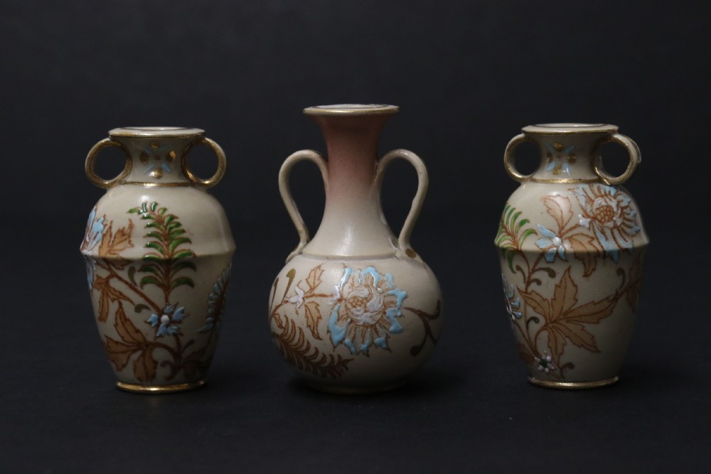 A set of three antique miniature cream ceramic vases featuring hand-painted floral motifs in blue, green, and brown with gilded highlights. View IX